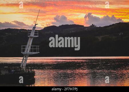 Malerischer und farbenfroher Sonnenuntergang über einem breiten Fluss der Drau in der Nähe von Maribor, mit Sonnenuntergang hinter kleinen grünen Hügeln im Hintergrund. Weiß Mo Stockfoto