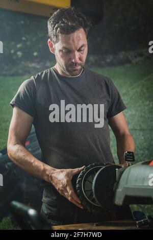 Ein professioneller Servicetechniker repariert einen Rasenmäher und montiert ein Vorderrad wieder. Mann repariert einen Mäher in einer Werkstatt Stockfoto