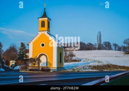 Eine kleine gelbe Kirche oder ein capel in Österreich zu sonniger Winterzeit. Typische Kapelle in Österreich oder im zentralen Teil europas, die von der Herbstsonne am Abend beleuchtet wird. Som Stockfoto