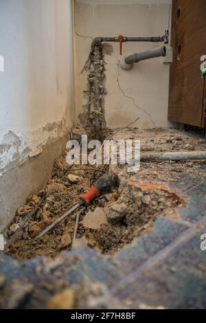 Kaputtes Wasserrohr in einer Wohnung. Sichtbares Loch im Boden mit Fliesen, altem Beton und Schutt. Baustelle beim Versuch, ein Wasser le zu beheben Stockfoto