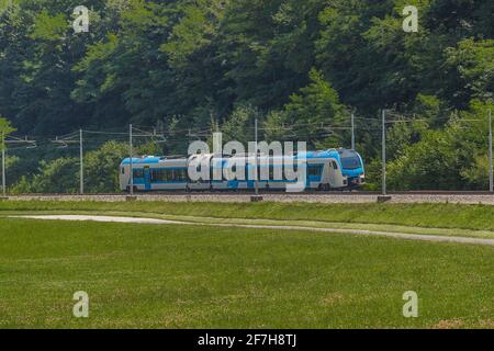 Moderner und neuer Passagier swiss Made Train in weiß und blau fährt an einem sonnigen heißen Tag auf einer zweigleisigen Bahnstrecke in ländlicher Umgebung. Stockfoto