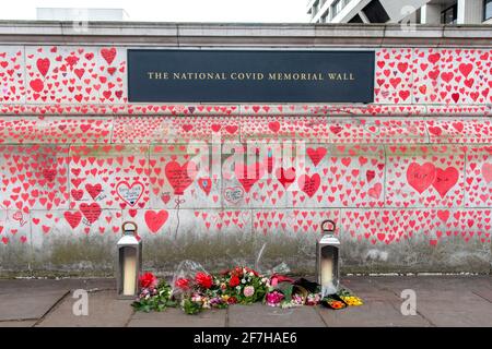 Kerzen und Blumengebete an der National Covid Memorial Wall.die Mauer grenzt an das St. Thomas' Hospital und wird mit 150000 Herzen handbemalt, um die britischen Covid-19-Opfer zu ehren.Sie ist über 700 Meter lang. Stockfoto