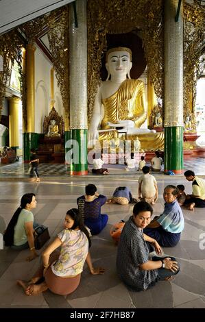 Menschen, die vor einer großen Buddha-Statue in der Shwedagon Pagode, Yangon, Myanmar, sitzen Stockfoto