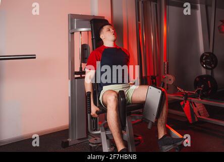 Ein junger Mann trainiert seine Beine, während er auf einem Simulator im Fitnessstudio sitzt. Krafttraining Stockfoto