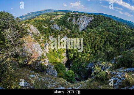 UNESCO-Weltkulturerbe Skocjanske jame mit einer weiten Fischauge aufgenommen. Blick auf die tiefe Schlucht mit Höhleneingang und Spazierwegen. Villa Stockfoto