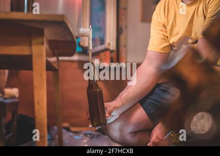 Home Craft Bierbrauerei. Letzter Schritt: Ein frisches IPA-Bier aus dem Fermenter in eine Flasche gießen. Hand hält eine Flasche mit selbstgemachtem blassem Bier. Stockfoto