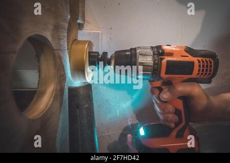 Ein Mann, der einen batteriebetriebenen Bohrer mit einem Kreissägebit verwendet, um ein Loch in eine Holzdiele zu bohren. Der Staubsauger ist sichtbar, um den überschüssigen Staub zu entfernen. Stockfoto