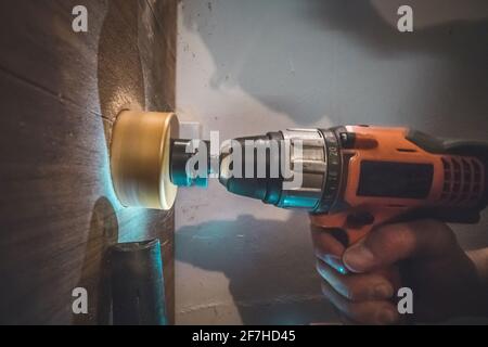 Ein Mann, der einen batteriebetriebenen Bohrer mit einem Kreissägebit verwendet, um ein Loch in eine Holzdiele zu bohren. Der Staubsauger ist sichtbar, um den überschüssigen Staub zu entfernen. Stockfoto