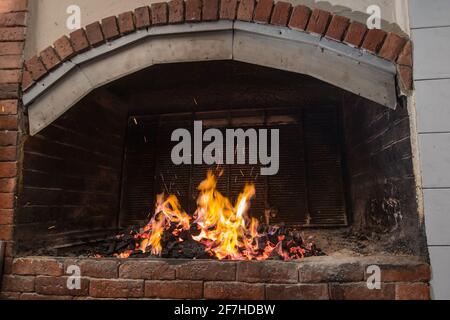 Ein großer offener Feuergrill, der mit Hilfe von Holzkohle erhitzt wird, Flammen fangen gerade an, bis zum Kamin zu steigen. Metallgitter warten darauf Stockfoto