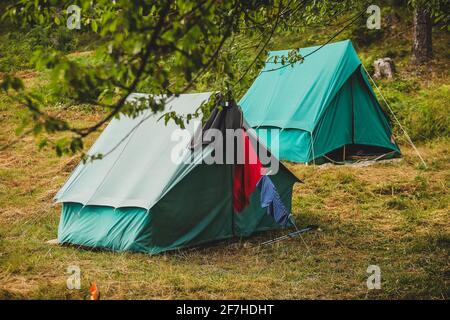 Zwei dreieckige Zelte in grüner Farbe, die in der Natur errichtet wurden. Einige Kleidungsstücke trocknen vor einer. Stockfoto