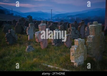 Furchterregend aussehender Friedhof in Serbien mit einem gruseligen Dorf, das am frühen Abend im nebligen Hintergrund gesehen wurde. Stockfoto