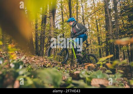 Biker, die im Herbst oder Winter mit einem modernen Elektrofahrrad oder Mountainbike in einem Wald bergauf fahren. Moderner E-Radfahrer im Wald. Stockfoto