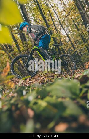 Biker, die im Herbst oder Winter mit einem modernen Elektrofahrrad oder Mountainbike in einem Wald bergauf fahren. Moderner E-Radfahrer im Wald. Stockfoto