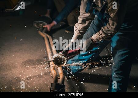 Man schneidet einen alten Auspuff oder Metallrohre mit Hilfe eines Winkelschleifers. Funken fliegen herum, wie ein Mann Winkelschleifer benutzt, Stockfoto