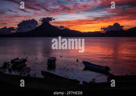 Panoramablick auf den Atitlan-See in Guatemala am Abend mit reichen Blumen des Sonnenuntergangs und einigen Booten im Vordergrund. Stockfoto