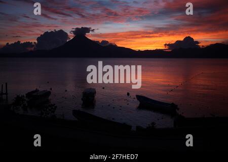 Panoramablick auf den Atitlan-See in Guatemala am Abend mit reichen Blumen des Sonnenuntergangs und einigen Booten im Vordergrund. Stockfoto