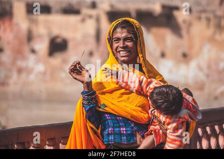 JAIPUR, Indien, 2. 2016. DEZEMBER: Eine Frau aus Indien, die ein Kind trägt und einen orangefarbenen Schal trägt und an einem sonnigen Tag lächelt. Stockfoto