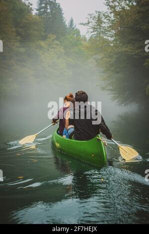 Rückansicht eines grünen Kanus in einem nebligen und nebligen Fluss zwischen den Bäumen. Gruselige und unheimliche Erkundung mit einem Kanu auf einem Fluss Krupa in Sloveni Stockfoto