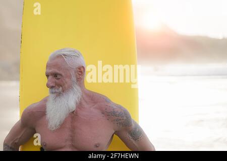 Sportlich bärtiger Mann trainiert mit Surfbrett am Strand. Ältere gesunde Menschen Lebensstil und Extremsportkonzept. Stockfoto