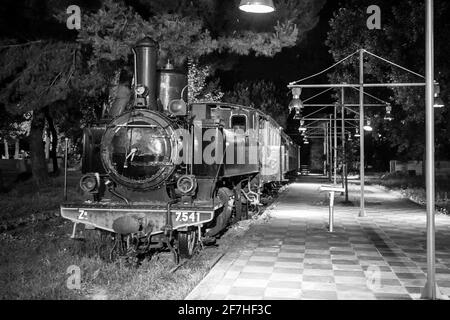 Alte Dampfeisenbahn in der Nacht geparkt als Außenausstellung von Eisenbahnen in einem Park in der griechischen Stadt Kalamata. Dampflokomotive mit Wagen in Par Stockfoto