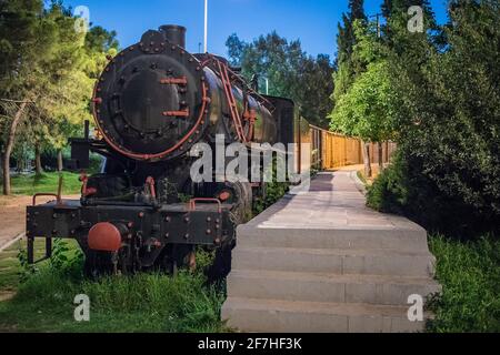 Alte Dampfeisenbahn in der Nacht geparkt als Außenausstellung von Eisenbahnen in einem Park in der griechischen Stadt Kalamata. Dampflokomotive mit Wagen in Par Stockfoto