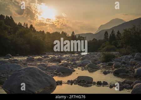 Schöner Sommerabend mit Sonne gerade untergehen behnd julischen alpen und Fluss in Resia Region oder Rezija, in der Nähe von Resciutta Dorf. Steine im W Stockfoto