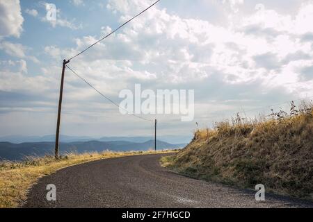 Panorama einer schönen Sommerlandschaft mit Sonne, Wolken und gelben Feldern in Frankreich. Ländliche landschaftlich schöne Asphaltstraße in einer Kurve sichtbar geht um die c Stockfoto