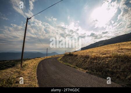 Panorama einer schönen Sommerlandschaft mit Sonne, Wolken und gelben Feldern in Frankreich. Ländliche landschaftlich schöne Asphaltstraße in einer Kurve sichtbar geht um die c Stockfoto