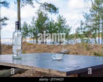 Mehrere Flaschen Bier auf dem Tisch. Müll, Müll, Müllhaufen im Wald mit kaputten Tisch. Nach einer Party draußen gelassen. Leere Flaschen, Alkohol. Alte Brunnenplatte als Tisch verwendet. Grillparty im Wald. Stockfoto