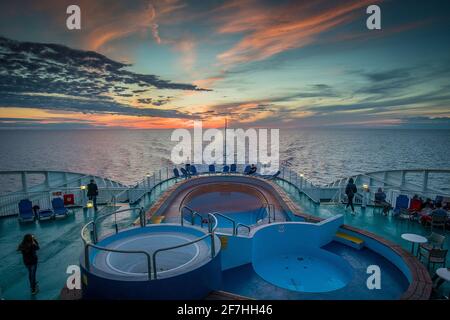 Abendpanorama der untergehenden Sonne von einem fahrenden Schiff aus gesehen. Sichtbare Spur, Wake oder Pfad und Pools auf einem Schiff während des Sonnenuntergangs. Romantischer Reiseabend Stockfoto