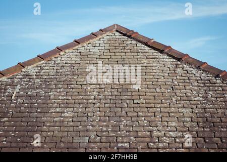 Ein Dreieck oder ein Hüftdach, das den Grat, Mörtel und Flechten auf den alten beschädigten traditionellen Steinschieferfliesen zeigt Stockfoto