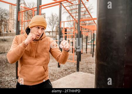 Junger Mann im Sportoutfit macht morgens Workout im Freien. Junger Mann beim Boxen auf dem Straßensportplatz. Fit und gesund bleiben Konzept Stockfoto