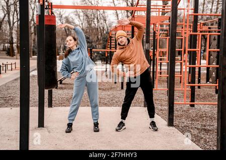 Junges Paar im Sportoutfit macht morgens Workout im Freien. Junge Männer und Frauen dehnen ihre Muskeln, bevor sie auf dem Straßensportplatz laufen Stockfoto
