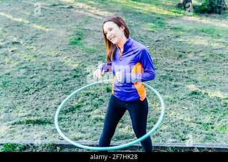 Schöne junge Frau tut Hula Hoop bei Sonnenuntergang in einem park Point Konzept Sport rhythmische Gymnastik Körperpflege Stockfoto