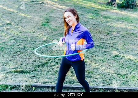 Schöne junge Frau tut Hula Hoop bei Sonnenuntergang in einem park Point Konzept Sport rhythmische Gymnastik Körperpflege Stockfoto