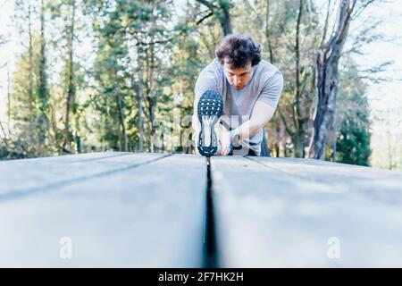 Junger erwachsener Mann, der sich in einem Park auf den Tisch streckt Laufkonzept Körperpflege Stockfoto
