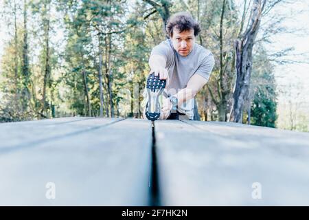 Junger erwachsener Mann, der sich in einem Park auf den Tisch streckt Laufkonzept Körperpflege Stockfoto