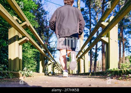 Rückansicht eines jungen Läufers, der durch einen bewaldeten Park läuft Auf einem Holzsteg im Frühjahr oder Sommer Concept Sport Persönliche Betreuung Stockfoto