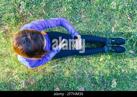 Luftaufnahme einer Frau, die auf der Smartwatch auf dem Boden schaut In einem Park mit Gras Blick auf Training Piste Konzept Sport und Technologie im Freien Stockfoto