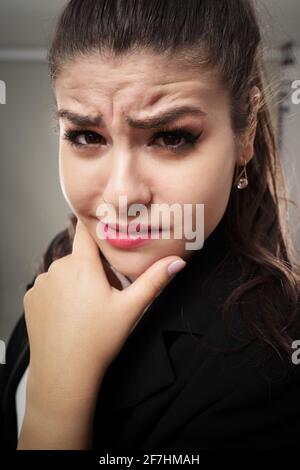 Zweifelhafte junge hispanische Geschäftsfrau mit der Hand am Kinn Stockfoto
