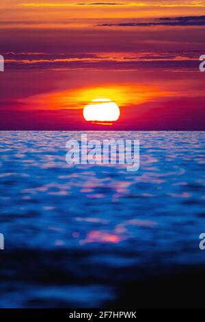 Farbenfroher Sonnenuntergang mit großer, heller Sonne unter der Meeresoberfläche. Sonnenuntergang am Meer, Sonnenaufgang am Meer, Meereslandschaft. Stockfoto