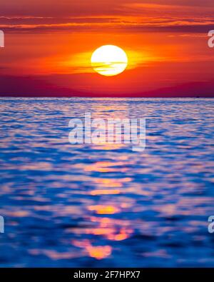 Heller Sonnenuntergang mit großer gelber Sonne unter der Meeresoberfläche. Stockfoto