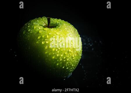 Grüner Apfel mit Wassertropfen auf schwarzem Hintergrund Stockfoto