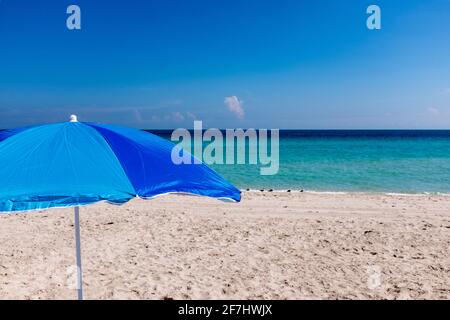 Ein blauer Sonnenschirm, eingerahmt vom azurblauen Wasser des Atlantiks vor South Beach, Miami Beach, Florida Stockfoto