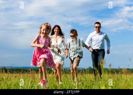Glückliche Familie - Mutter, Vater, Kinder - laufen über eine grüne Wiese im Sommer treten einen Fußball Stockfoto