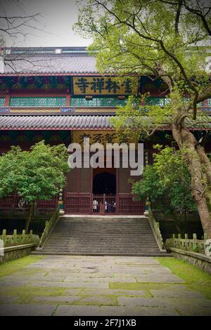 Einer der Tempel im Lingyin Tempel liegt in Hangzhou, Zhejiang, China, mit hölzernen Eingangstür, vielen Stufen, einem alten Gebäude und grünen Bäumen. Stockfoto