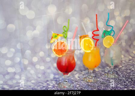 Drei große Gläser mit Limetten-, Grapefruit- und Orangensaft mit Eis, Trinkhalmen und Scheiben Zitrusfrüchten auf einem grauen abstrakten Hintergrund. Nahaufnahme. Stockfoto