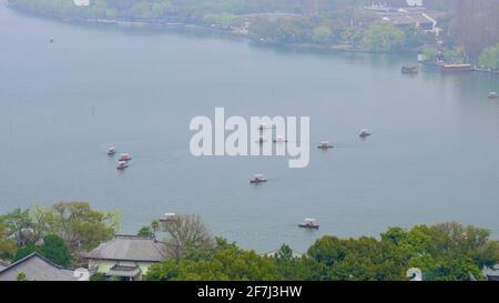 Kleine Boote, die weit weg auf dem West Lake mit Bäumen am Seeufer fahren. Stockfoto