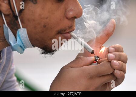 Ein Mann, der außerhalb von ‘Weed World Candies' sitzt, raucht Cannabis, nach Gov. Andrew Cuomo unterzeichnete ein Gesetz zur Legalisierung von Marihuana für den Freizeitkonsum, New York, NY, 7. April 2021. Während medizinische Marihuana-Verteilungsstellen reguliert sind, wurde der Zeitplan für die Eröffnung von Verteilungsstellen für Freizeitangebote noch nicht festgelegt, da die Regulierung und die Besteuerung von Verkäufen noch nicht abgeschlossen sind. Die Legalisierung von Marihuana für den Freizeitkonsum erlaubt Personen ab 21 Jahren, bis zu drei Unzen Cannabis und Rauch in der Öffentlichkeit zu transportieren und zu verwenden, wo Rauchen erlaubt ist. (Foto von Anthony Behar/Sipa USA) Stockfoto