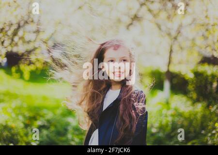 Kleines Mädchen in schwarzer Jacke, das in der Frühlingskirsche steht Garten Stockfoto